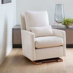 a white chair sitting on top of a hard wood floor next to a vase filled with flowers