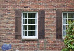 two windows with wooden shutters on the side of a brick building