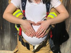 a woman in firefighter gear holding her stomach with both hands while standing next to a wooden fence