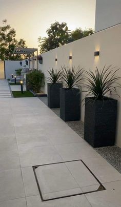 three black planters sitting on the side of a building next to a sidewalk with grass