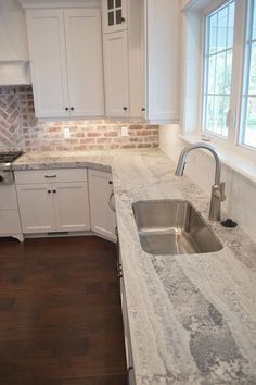 a kitchen with white cabinets and marble counter tops, along with a stainless steel sink