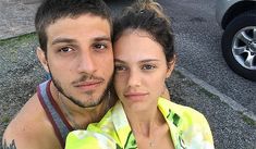 a young man and woman posing for a photo together in front of a parked car