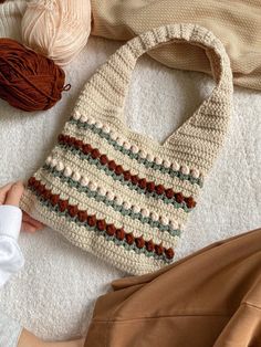 a crocheted bag sitting on top of a white rug next to yarn balls