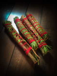 three bundles of cinnamon sticks wrapped in twine and tied with red string on top of a wooden table