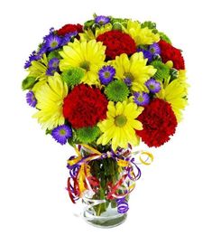 a vase filled with lots of colorful flowers on top of a white table next to a ribbon