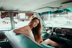 a beautiful young woman sitting in the driver's seat of an old fashioned car