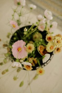 flowers in a black vase sitting on a table top with white and pink flowers around it