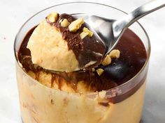 a spoon with some ice cream and chocolate in it on top of a glass bowl