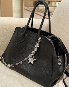 a black handbag sitting on top of a white couch next to a chair with a chain hanging from it