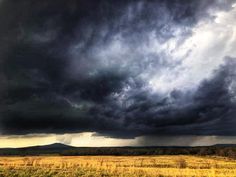 the sky is very dark and cloudy over an open field