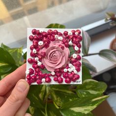 a hand holding up a pink flower with white and red beads on it's petals