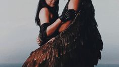 two people dressed in native american clothing with wings on their shoulders and arms wrapped around each other