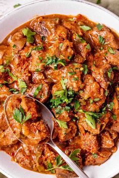 a white bowl filled with meat and garnished with parsley on the side