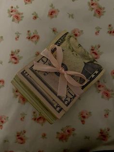 a stack of money tied with a pink ribbon on top of a floral print sheet