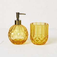 a yellow glass soap dispenser next to a yellow glass cup on a white surface