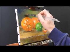 a person holding a knife in front of a painting with oranges and limes on it