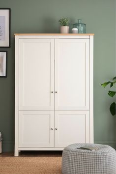 a white armoire sitting next to a green wall and potted plant on top of it