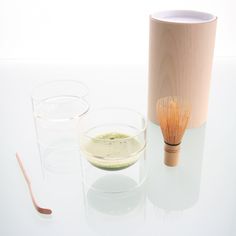 a whisk in a bowl next to two glasses and a wooden spoon on a white surface