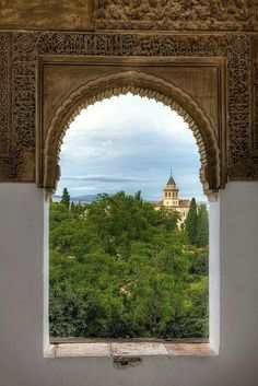 an arched window with a view of trees and buildings in the distance, looking out over a lush green valley