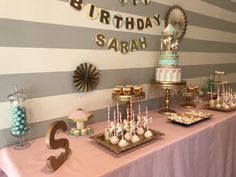 a table topped with lots of cakes and desserts next to a wall covered in striped walls