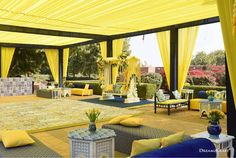 an outdoor area with yellow drapes and blue couches, tables, and rugs