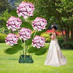 a woman in a wedding dress standing next to a tall plant with pink flowers