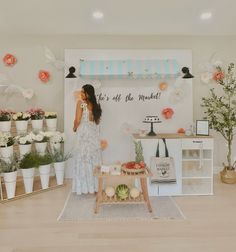 a woman standing in front of a display with flowers and fruit on the table next to it