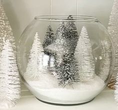 snow covered trees in a glass bowl sitting on a shelf next to other christmas decorations