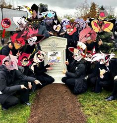 a group of people wearing masks sitting on top of a grass covered field next to a grave