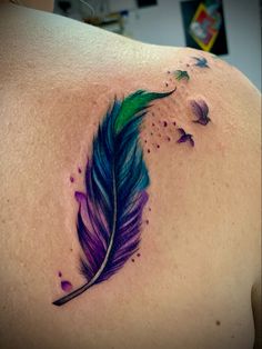 a colorful feather tattoo on the back of a woman's shoulder