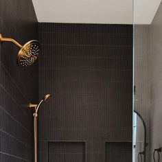 a bathroom with black tile and gold shower faucet in the corner, next to a walk - in shower