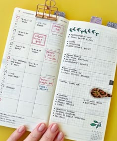 a hand holding an open planner on top of a yellow table