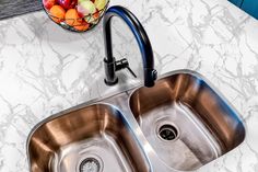 a kitchen sink with two faucets next to it and a bowl of fruit on the counter