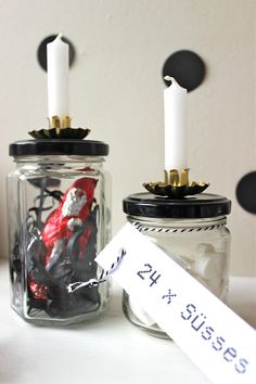 two mason jars with candles and stickers in them sitting on a table next to each other