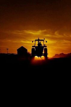 a tractor is silhouetted against the setting sun on a farm in an open field