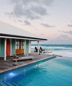 two people sitting on the edge of a pool next to a house with a surfboard in it