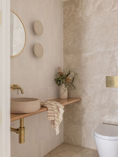 a white toilet sitting next to a wooden shelf in a bathroom under a round mirror