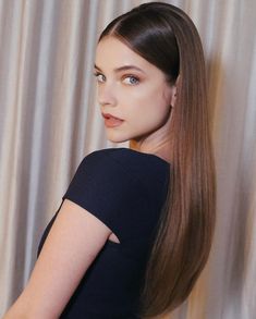 a woman with long hair standing in front of a curtain wearing a black dress and blue eyeshadow