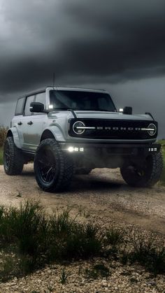 a white truck driving down a dirt road under a cloudy sky