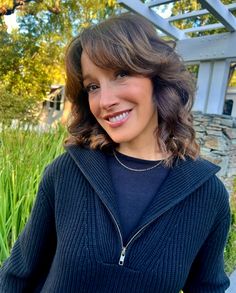 a woman is smiling and posing for the camera with her hand on her hip while wearing a black sweater