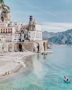 people are on the beach in front of an old building and some water with mountains in the background