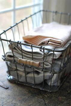 a basket filled with folded clothes on top of a wooden floor next to a window