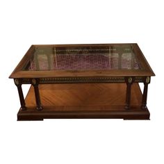 a glass top coffee table with wooden legs and an intricate design on the bottom shelf