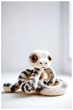 a crocheted snake sitting on top of a white table next to a window