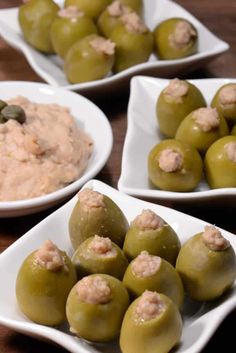 four white plates filled with green olives and hummus