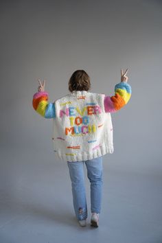 a woman walking with her hands in the air while wearing a sweater that says be kind of cool