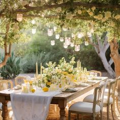 an outdoor dining table set up with white and yellow flowers, candles and greenery