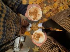 two people standing next to each other holding cups with drinks in them on top of leaves