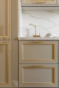 a white and gold kitchen with marble counter tops, cabinets, and brass pulls on the doors