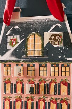 a paper house with christmas decorations on the roof and windows, hanging from a red ribbon